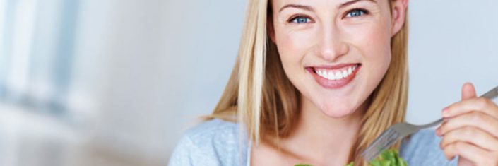 Mulher sorrindo e comendo salada | Os benefícios da alimentação saudável para a pele