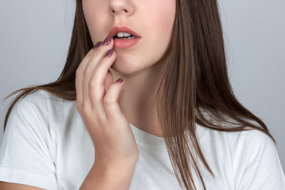 Menina com herpes na boca tocando a ferida