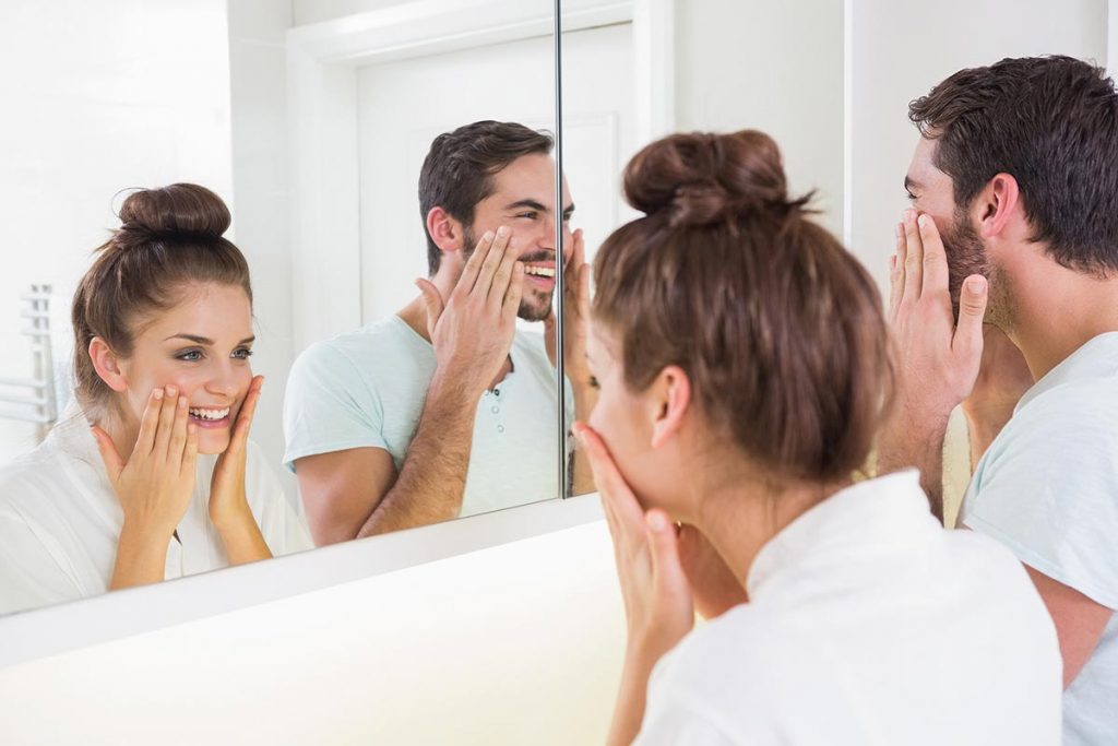 Homem e mulher olhando no espelho passando produtos na pele