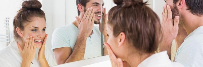 Homem e mulher olhando no espelho passando produtos na pele