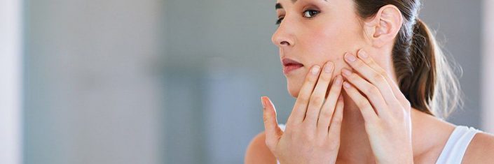 Mulher adulta olhando o rosto com acne no espelho