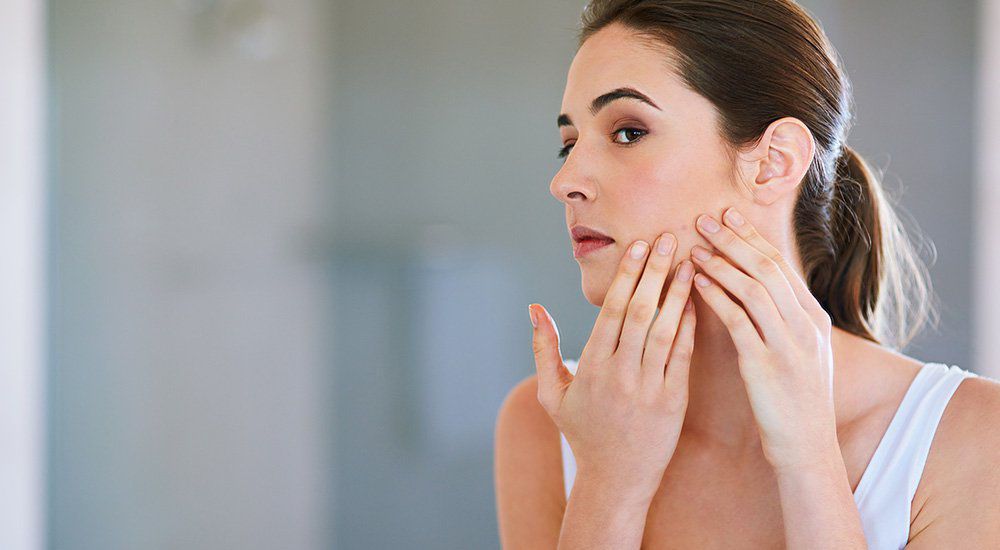 Mulher adulta olhando o rosto com acne no espelho